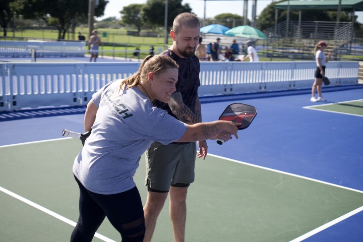 Coach showing an adult player a pickleball paddle grip on court