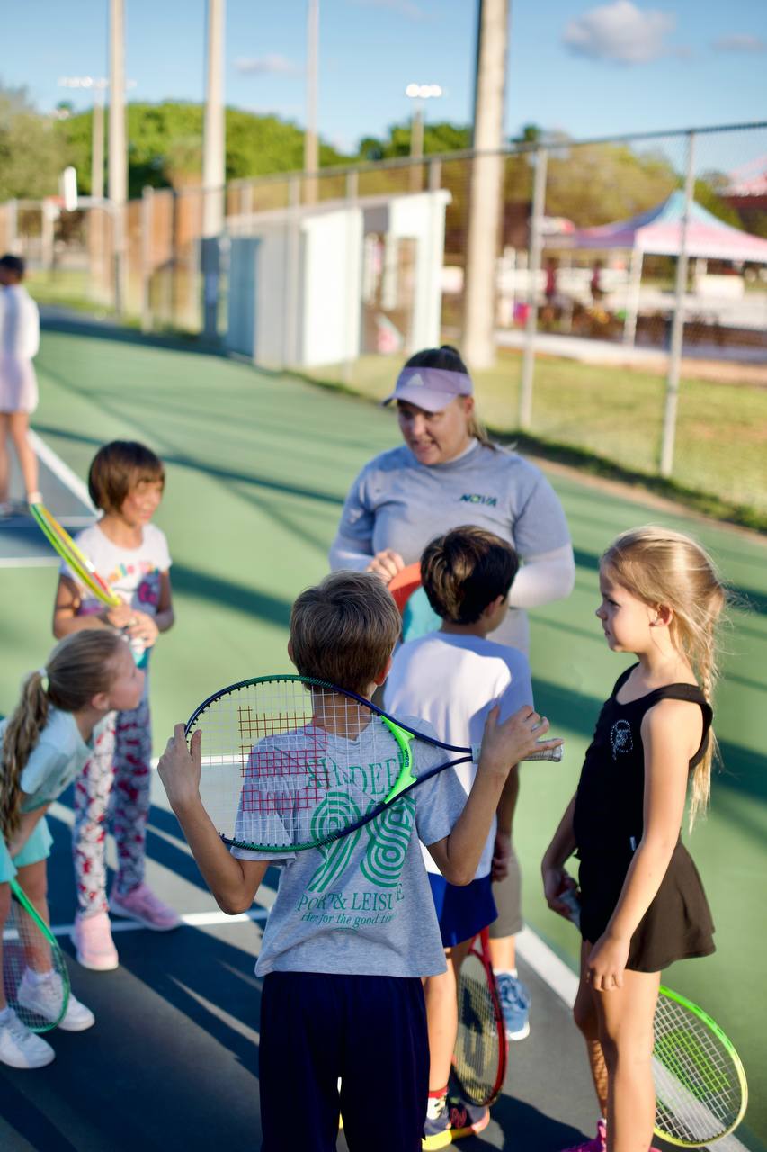 Coach talking to a group of children with rackets on court