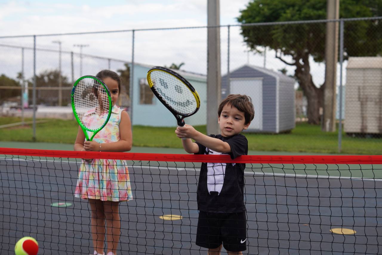 Two small children practising volleys over a low mini-tennis net