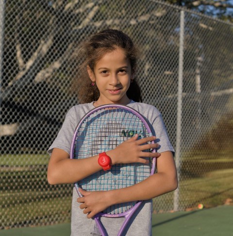 Girl hugging her racket by the court fence
