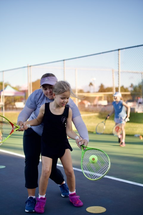 Coach guiding a young girl's forehand swing